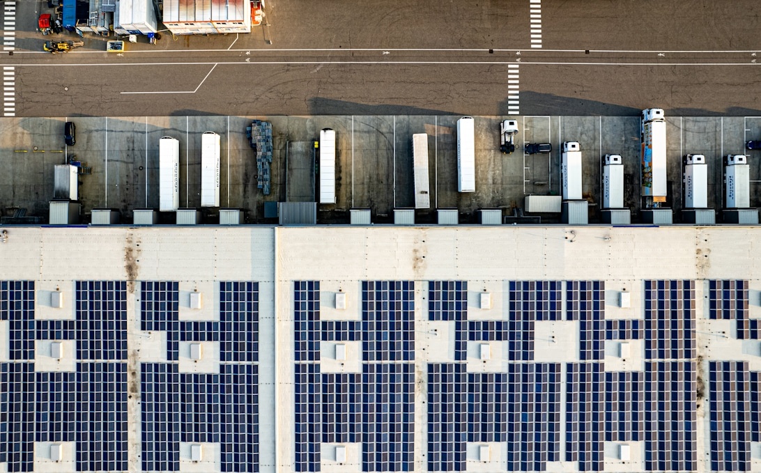 Luftaufnahme eines Versandterminals mit großen blauen Solaranlagen auf den Dächern der Lagerhallen.