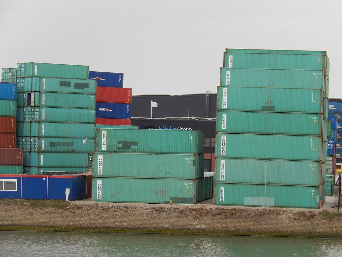 Ein Containerterminal mit gestapelten grünen, blauen und roten Containern in der Nähe eines Wasserwegs.